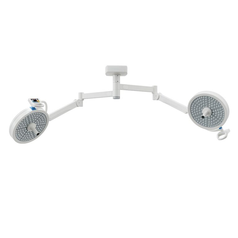 A dual-head Komax LED surgical light system with a white heat-efficient aluminum body, featuring circular LED arrays and central handles, mounted on a ceiling-integrated German technology arm system