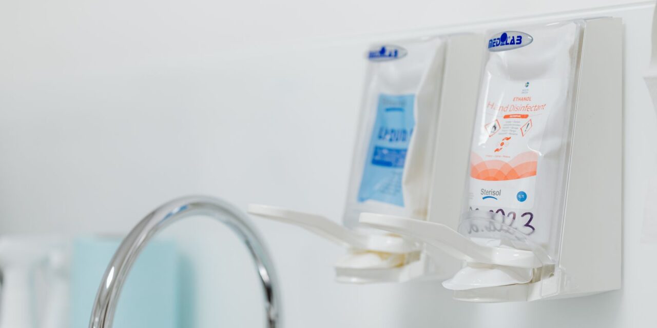 Stainless steel faucet with wall-mounted soap and disinfectant dispensers in a clinical wash area