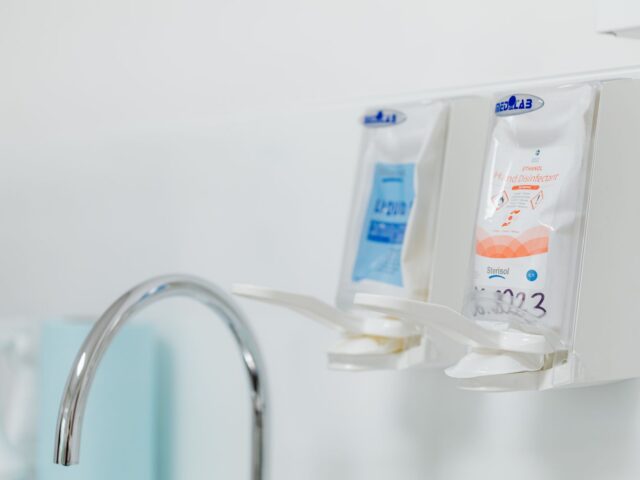 Stainless steel faucet with wall-mounted soap and disinfectant dispensers in a clinical wash area