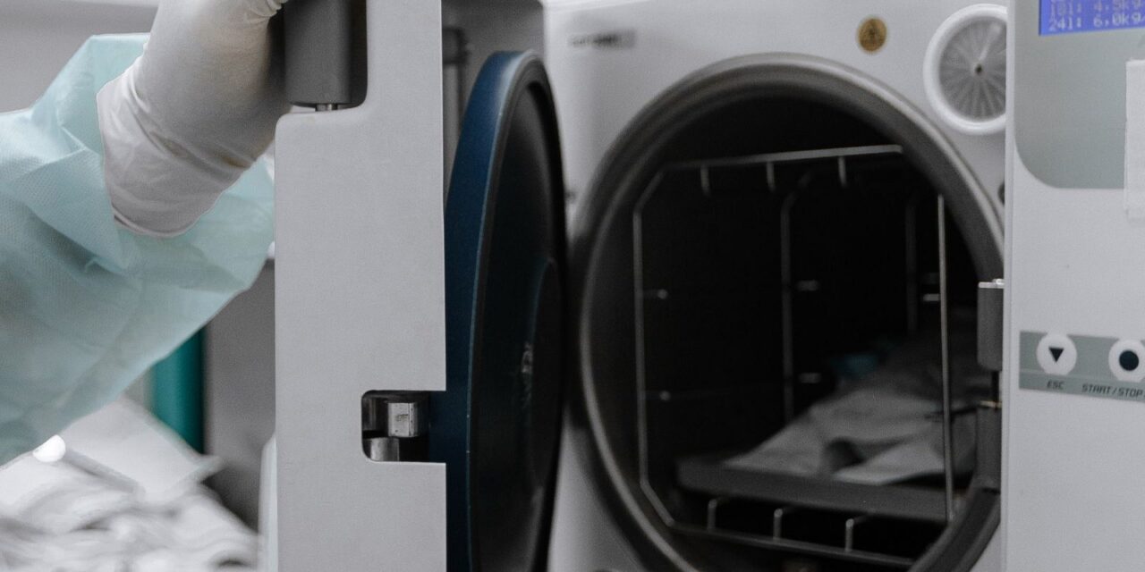 Gloved hand opening the door of a medical autoclave loaded with sealed sterilization pouches
