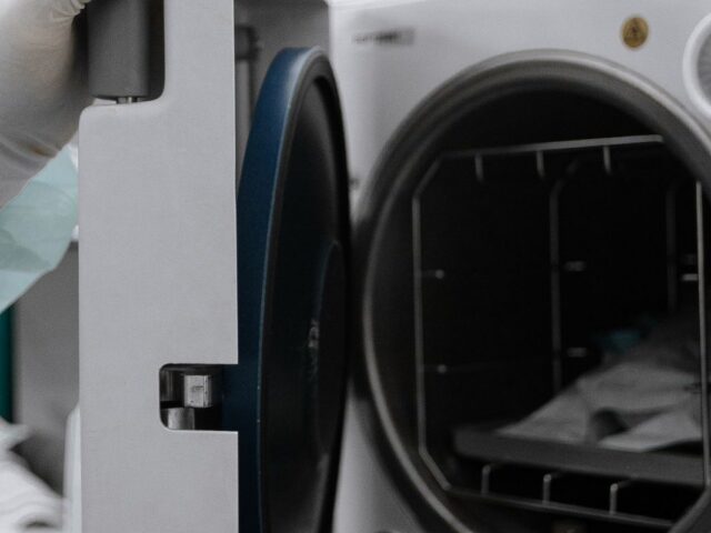 Gloved hand opening the door of a medical autoclave loaded with sealed sterilization pouches