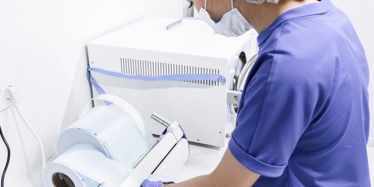 Technician in scrubs and cap operating low-temperature sterilization equipment in a laboratory