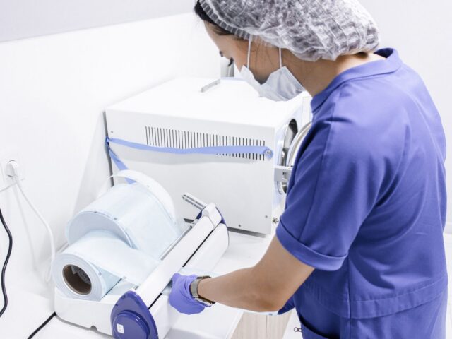 Technician in scrubs and cap operating low-temperature sterilization equipment in a laboratory